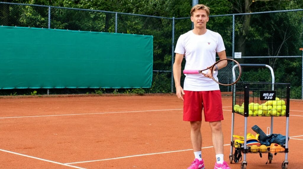 Erik Faneker op de tennisbaan met racket en ballenkar
